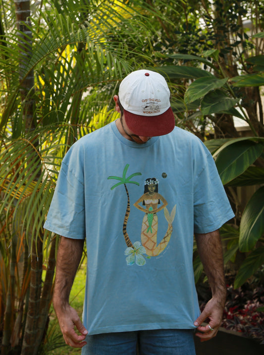 Man wearing a blue t-shirt with a tropical mermaid design in a garden setting