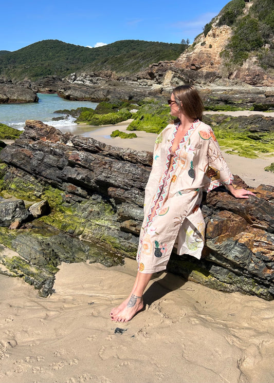 Woman in a floral kimono standing on a rocky beach with mountains in the background