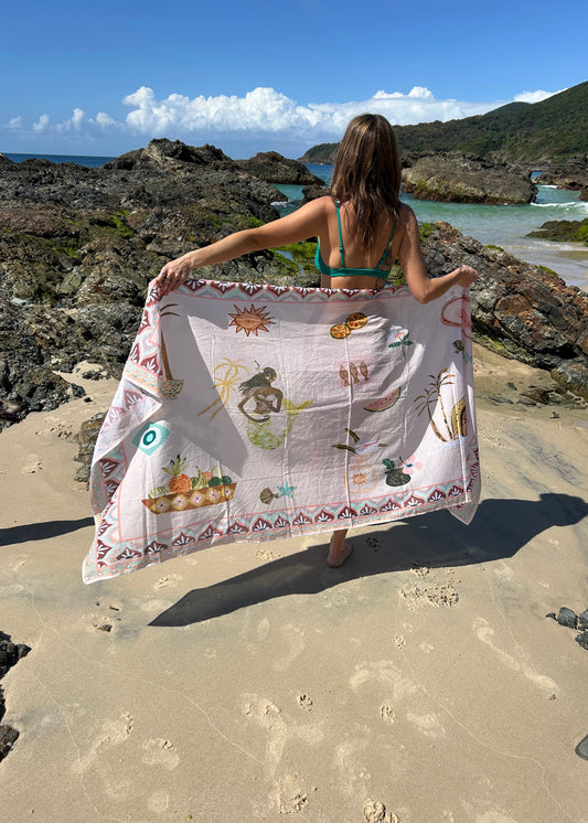 Person holding a colourful sarong on a rocky beach with clear blue sky.