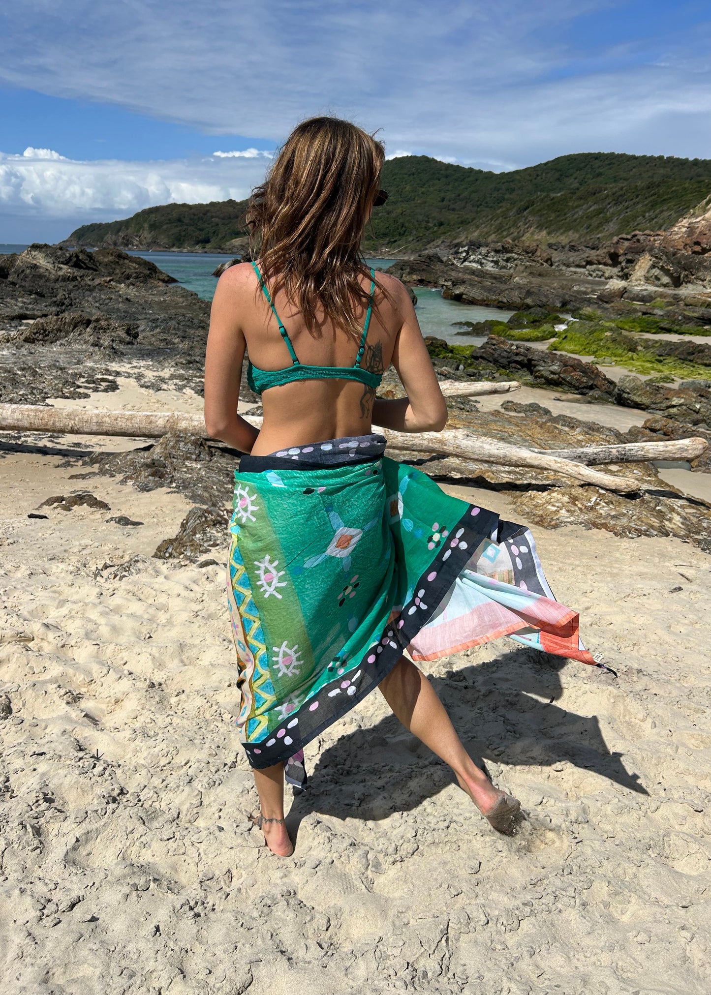 Person on a rocky beach with a scenic view of water and sky wearing a sarong