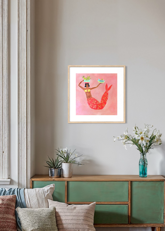 Sue fantini mermaid Framed artwork ofon a wall above a green cabinet with decorative items.