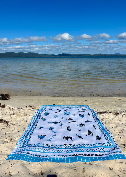 Beach towel with milagros patterns on a sandy beach with ocean and sky in the background