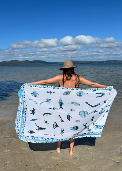 Person on a beach holding a blue and white Milagros sarong by sue fantini