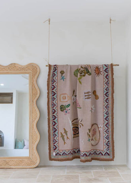 Decorative blanket from good throw co / sue fantini with mermaid patterns hanging on a rack against a white wall.