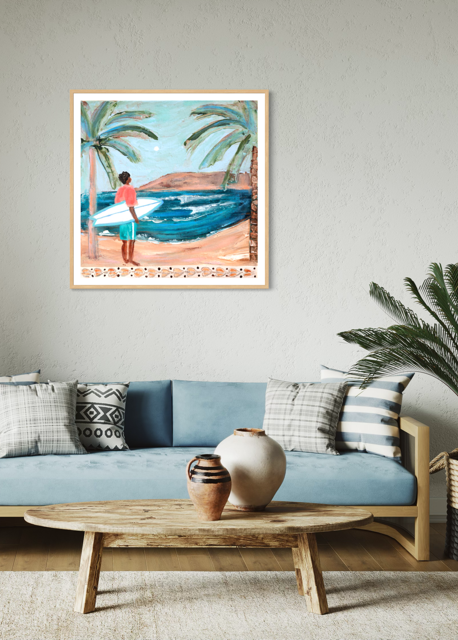 A framed art print depicting a beach scene with palm trees, blue ocean waves, and a person standing on the sand, displayed on a light gray wall above a blue sofa in a styled living room.