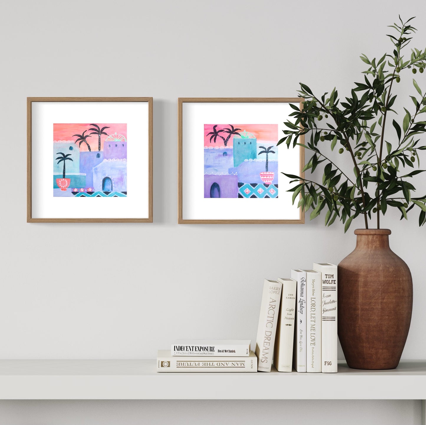 Set of two Moroccan art prints in pinks, orange, violet and teal framed in timber on wall with vase and book